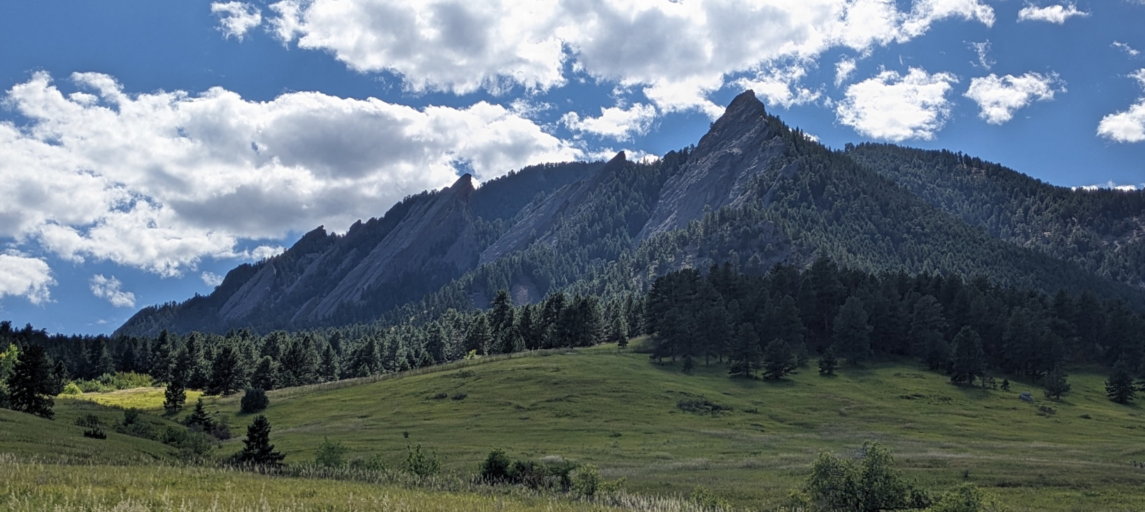 a range of mountains that look like irons at 45-degree angles, a blue sky and green grass